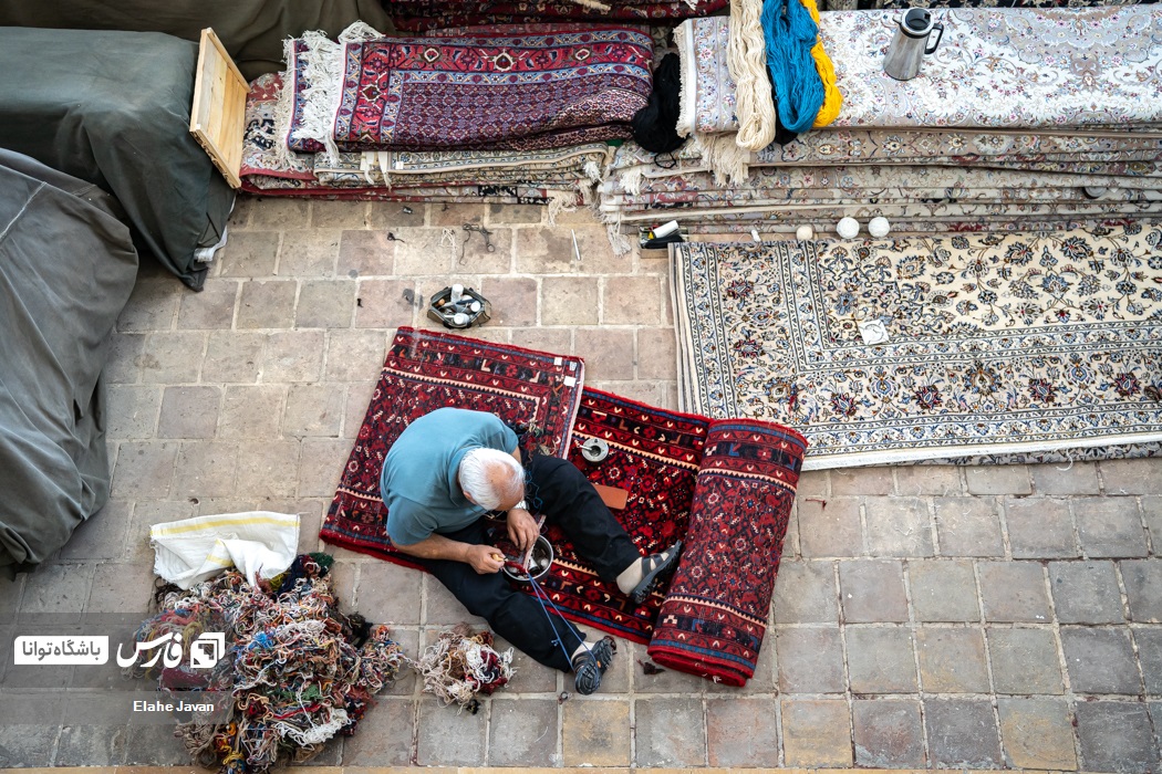 مردی میانسال در حال رفو کردن یک فرش قدیمی است